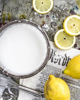 Zuckerguss in einer Schale neben ganzen und aufgeschnittenen Zitronen