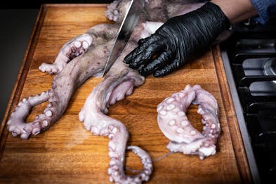 Tintenfisch-Tentakel werden mit einem großen Messer vom Rumpf des Tieres getrennt.