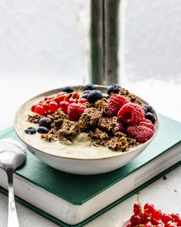 Joghurt mit selbstgemachtem Granola und Beeren in einer Schale mit Löffel auf Fensterbank