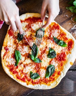 Pizza Margherita auf Holzbrett mit Händen, die Besteck halten