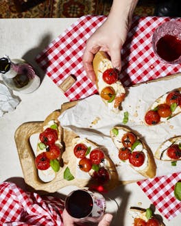 Mehre Ciabattastücke belegt mit Burrata und Tomaten auf einer Platte. Links und rechts sind zwei Hände.