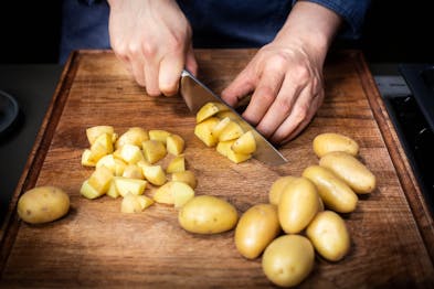 Kartoffeln werden auf einem Holzbrett mit einem großen Messer gewürfelt