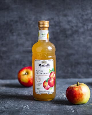 Flasche Apfelessig und Äpfel auf grauem Hintergrund
