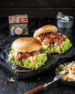 Zwei üppig belegte Burger mit Salat, Möhren und Thunfisch in Barbecue-Sauce sind auf schwarzem Untergrund präsentiert