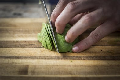 Eine halbe Avocado wird auf einem Holzbrett mit einem Messer  in feine Streifen geschnitten