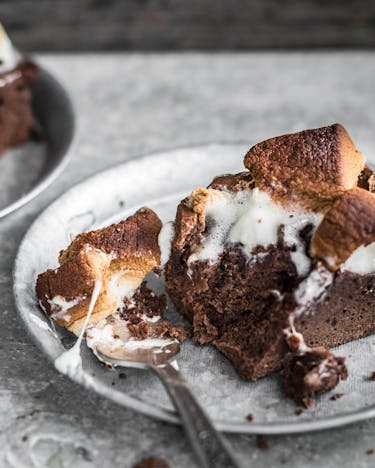 Zwei Teller mit Nuss-Nugat-Brownies und Marshmallows neben einer Kuchengabel