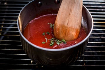 In einem Topf sind passierte Tomaten mit Kräutern und einem Holz-Kochlöffel