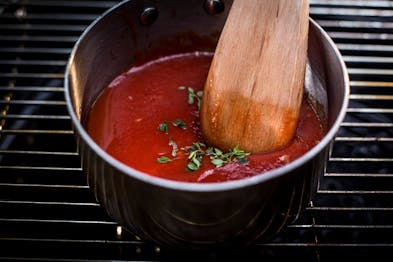 In einem Topf sind passierte Tomaten mit Kräutern und einem Holz-Kochlöffel