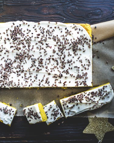 Angeschnittener Kürbisblechkuchen mit weißem Frosting und Kakaonibs auf Backpapier