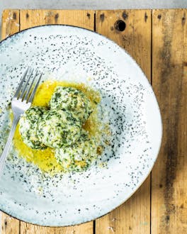 Malfatti – Ricotta-Spinat-Nocken in brauner Butter auf Teller auf Holztisch