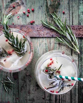 Wodka-Cocktail mit Traubensaftschorle, Birnensaft-Eiswürfeln und frischem Rosmarin in runden Gläsern auf Holzuntergrund.
