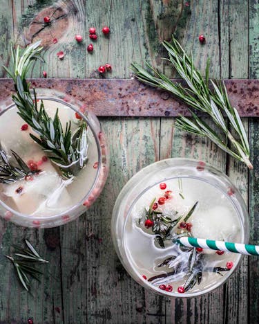Wodka-Cocktail mit Traubensaftschorle, Birnensaft-Eiswürfeln und frischem Rosmarin in runden Gläsern auf Holzuntergrund.