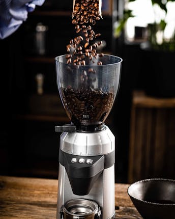 Kaffeebohnen werden aus der Packung direkt in eine elektrische Kaffeemühle gegeben