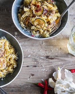 Pasta mit Thunfisch und Zucchini in zwei Porzellanschüsseln auf hellem Holzuntergrund