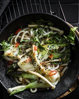 In einer schwarzen Schüssel liegen Udon-Nudeln mit Gemüse und Misopaste