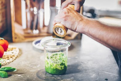 Grüne Pesto im Glas wird mit Pfeffer abgeschmeckt.