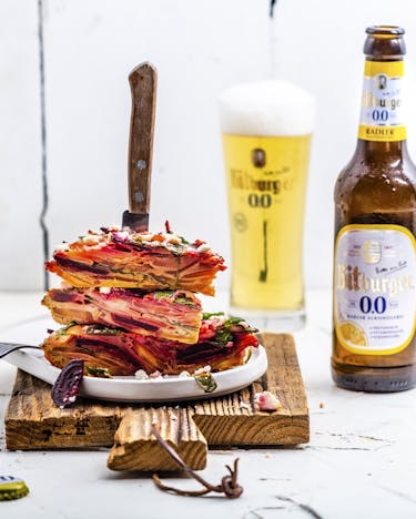 Rote-Bete-Frittata mit Wurzelgemüse auf Teller gestapelt mit Messer und alkoholfreies Bier im Hintergrund