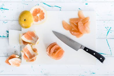 Auf einem weißen Brett liegen Grapefruit-Filets und der Küchenabfall der restlichen Grapefruit mit einem Küchenmesser.