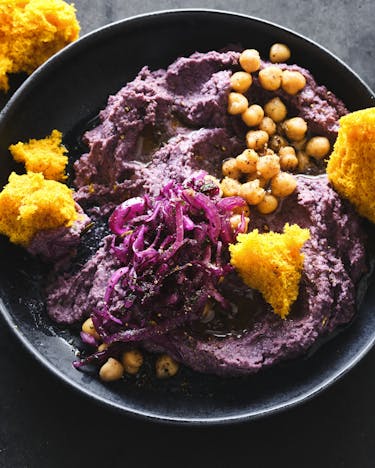 Eine Schale mit violettem Rotkohl-Hummus und goldgelbem Curry-Biscuit