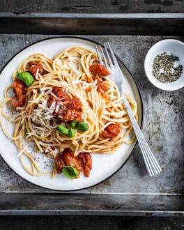 Spaghetti mit Tomatensoße auf einem weißen Teller auf einem Metalltablett.