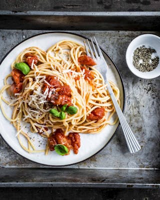 Spaghetti mit Tomatensoße auf einem weißen Teller auf einem Metalltablett.