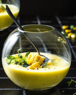 In einem Kugelglas ist die gelbe kalte Suppe, die mit Mais und Kresse dekoriert ist, serviert