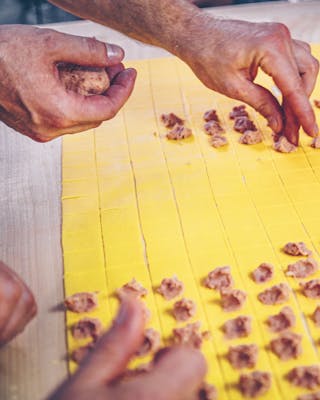 Füllung für selbst gemachte Tortellini wird auf kleinen Teigquadraten verteilt