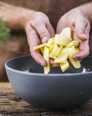 Hände legen Kartoffelsticks in eine Schale mit kaltem Wasser