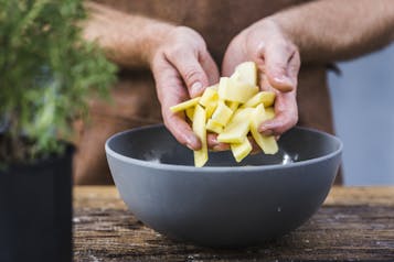 Hände legen Kartoffelsticks in eine Schale mit kaltem Wasser