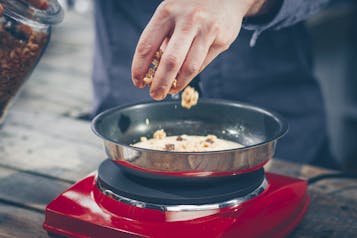 Pancake in einer Pfanne auf einer Kochplatte wird mit Schokomüsli bestreut