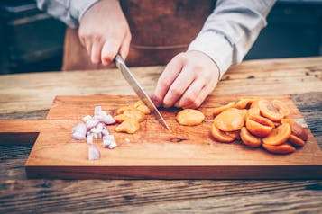 Aprikosen werden auf einem Holzbrett in Stücke geschnitten, daneben liegt gewürfelte Zwiebel