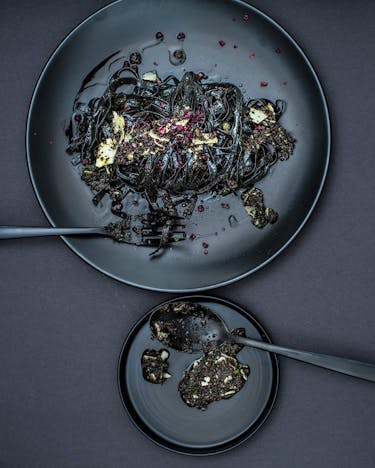 Schwarze Pasta mit Oliven-Majoran-Pesto auf schwarzem Teller und schwarzem Untergrund