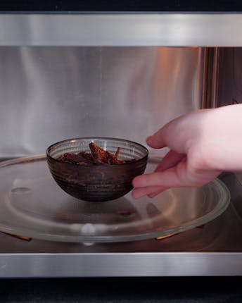 Eine Glasschale mit gehackter Schokolade wird zum Schmelzen in die Mikrowelle gestellt