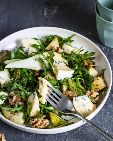 Salat mit Rucola, Birne und Walnuss mit Gorgonzola in weißer Schale vor dunklem Hintergrund