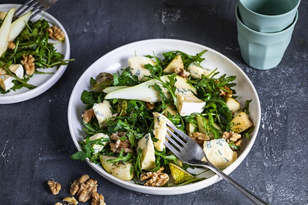 Salat mit Rucola, Birne und Walnuss mit Gorgonzola in weißer Schale vor dunklem Hintergrund