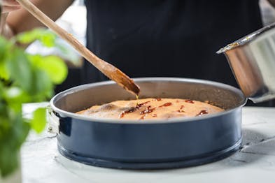 Hände verteilen mit Kochlöffel Sirup auf einen Kuchen in einer Springform